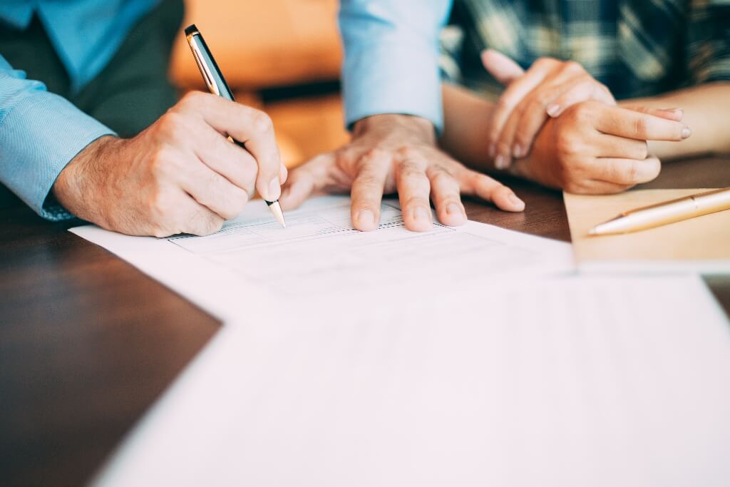 Man in a shirt signing a piece of paper whilst a woman watches